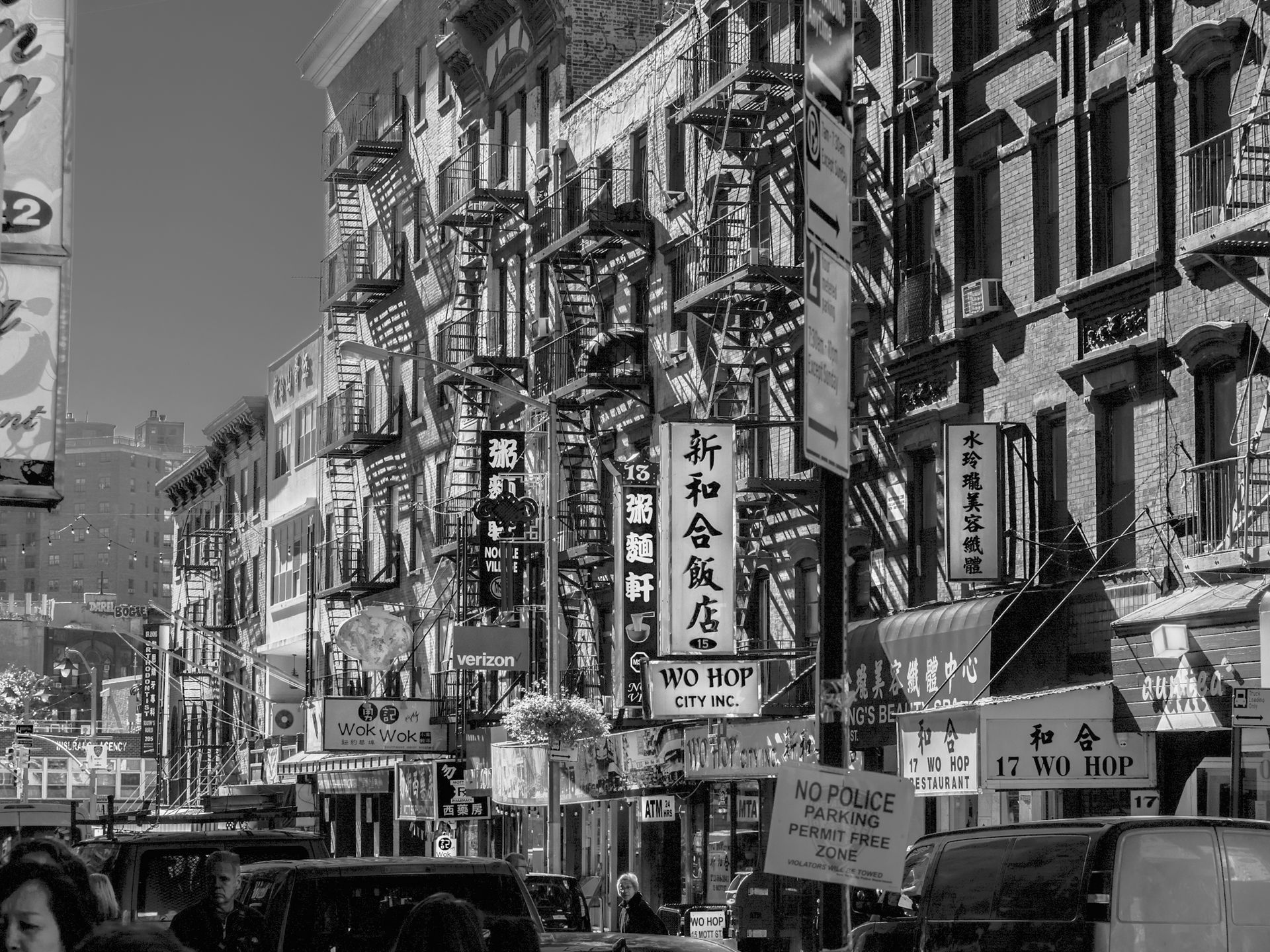A crowded street in NYC's Chinatown with tall brick buildings, fire escapes, and many vertical Chinese restaurant signs.