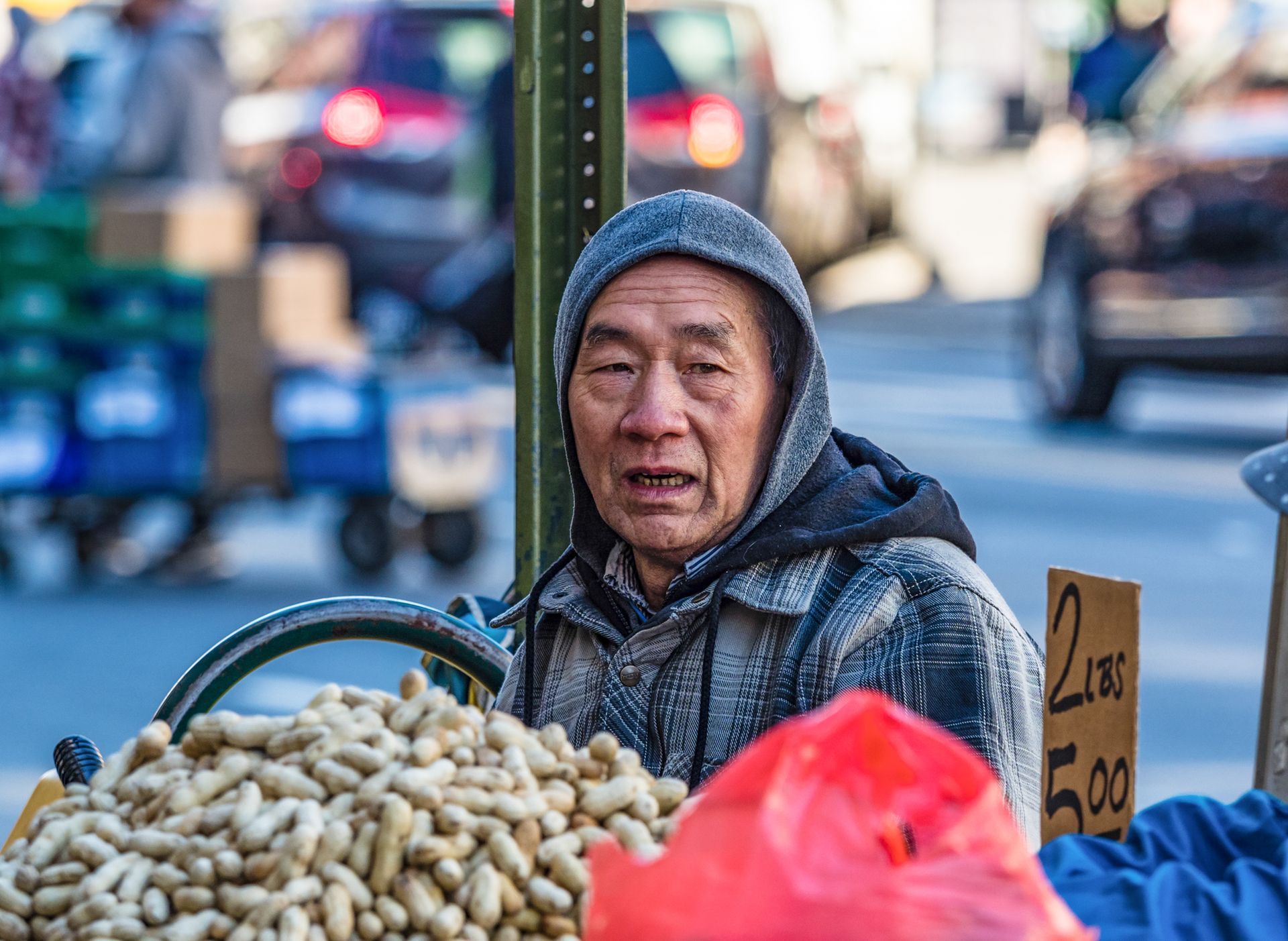 A person in a gray hooded jacket behind a stall filled with peanuts
