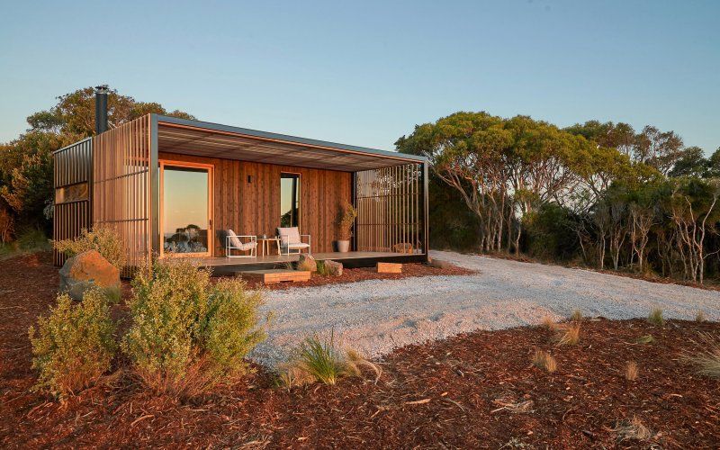 A small wooden house is sitting on top of a dirt hill surrounded by trees.