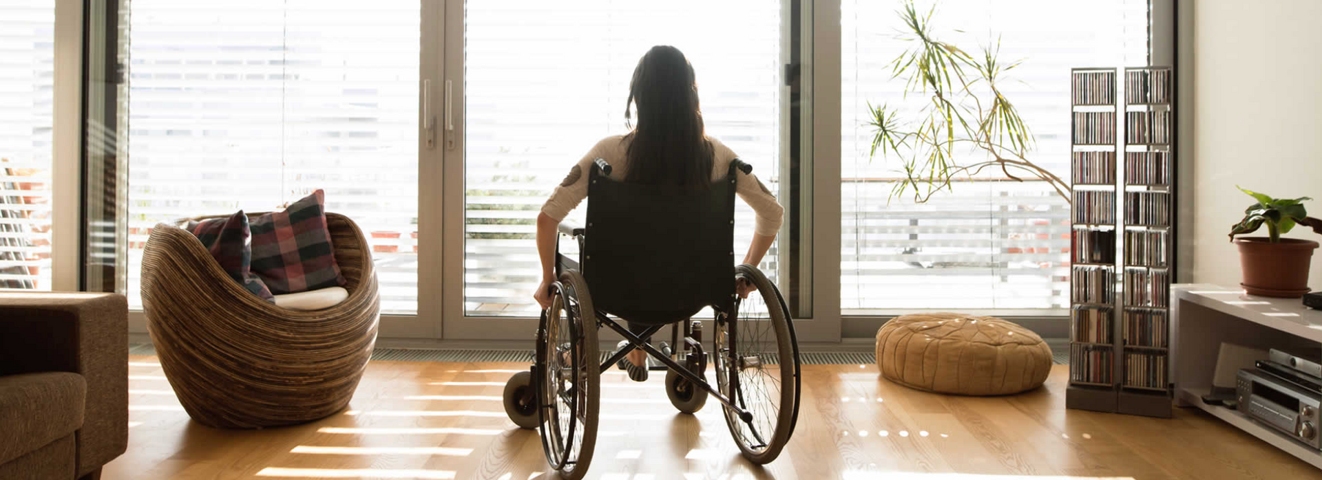 A woman in a wheelchair is looking out of a window in a living room.