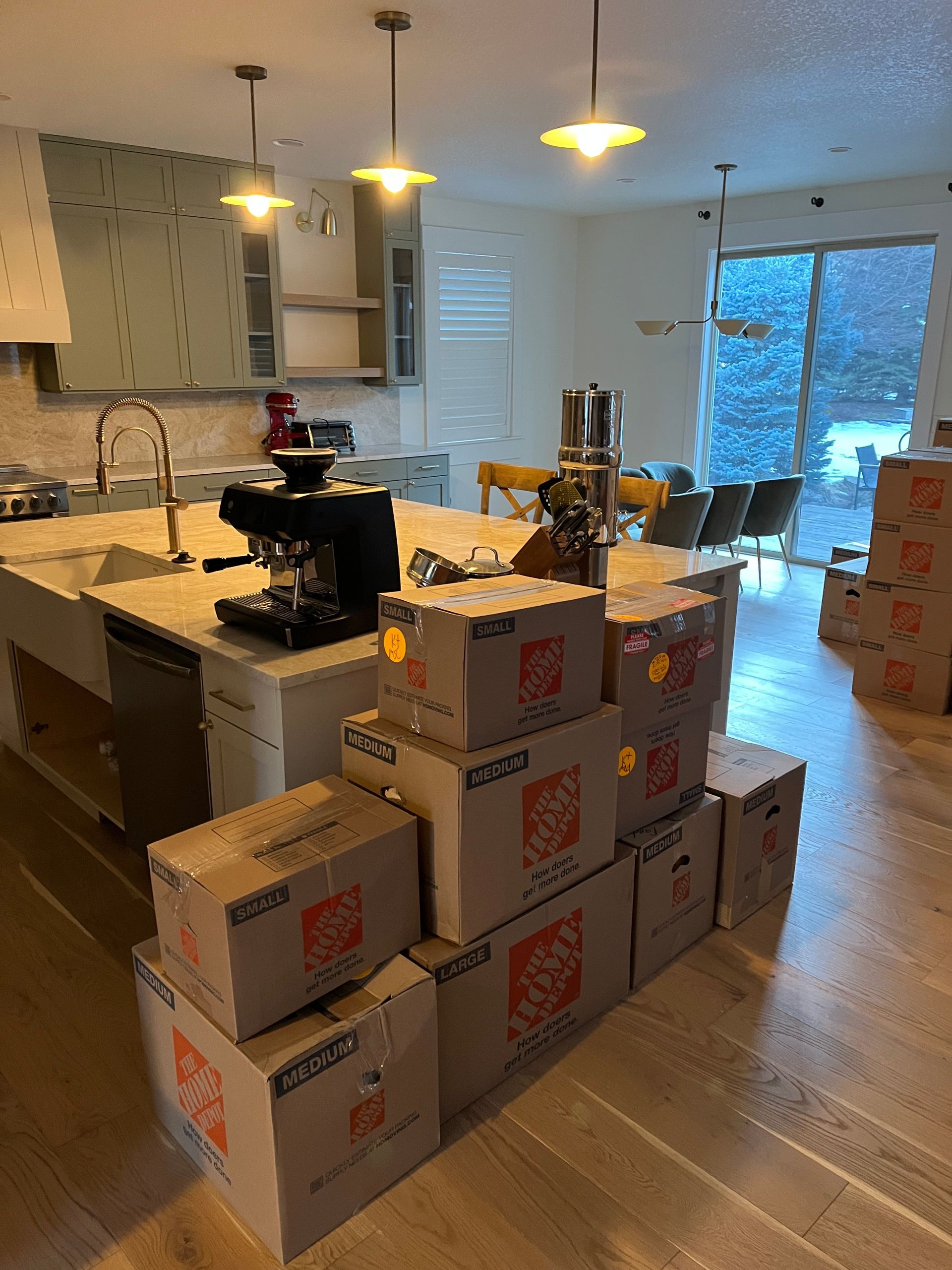 Kitchen with stacked moving boxes on the floor, a countertop, pendant lights, and a sliding glass door to snowy trees