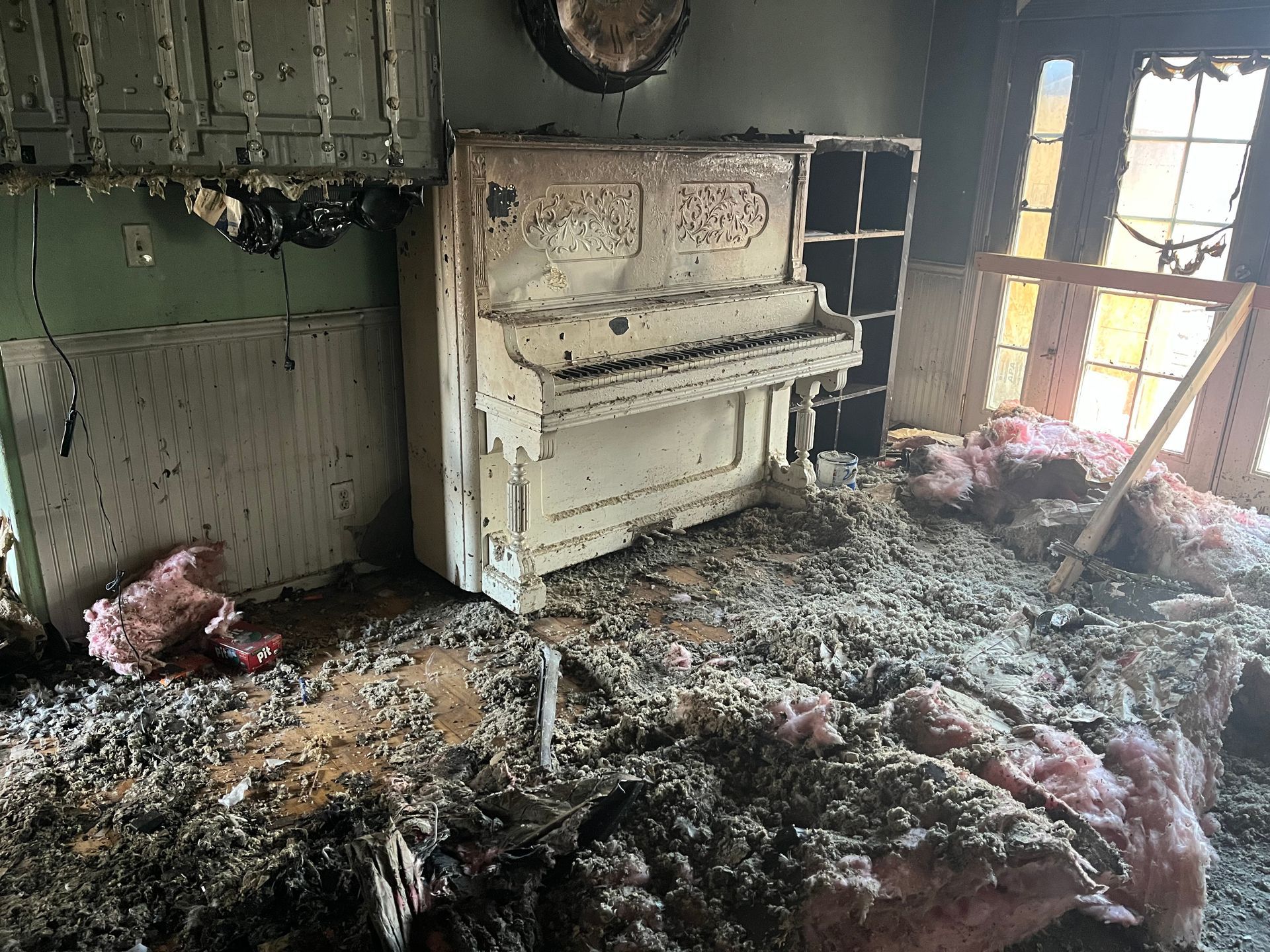 Fire-damaged room with a burned white piano amid heavy smoke and charred debris on the floor