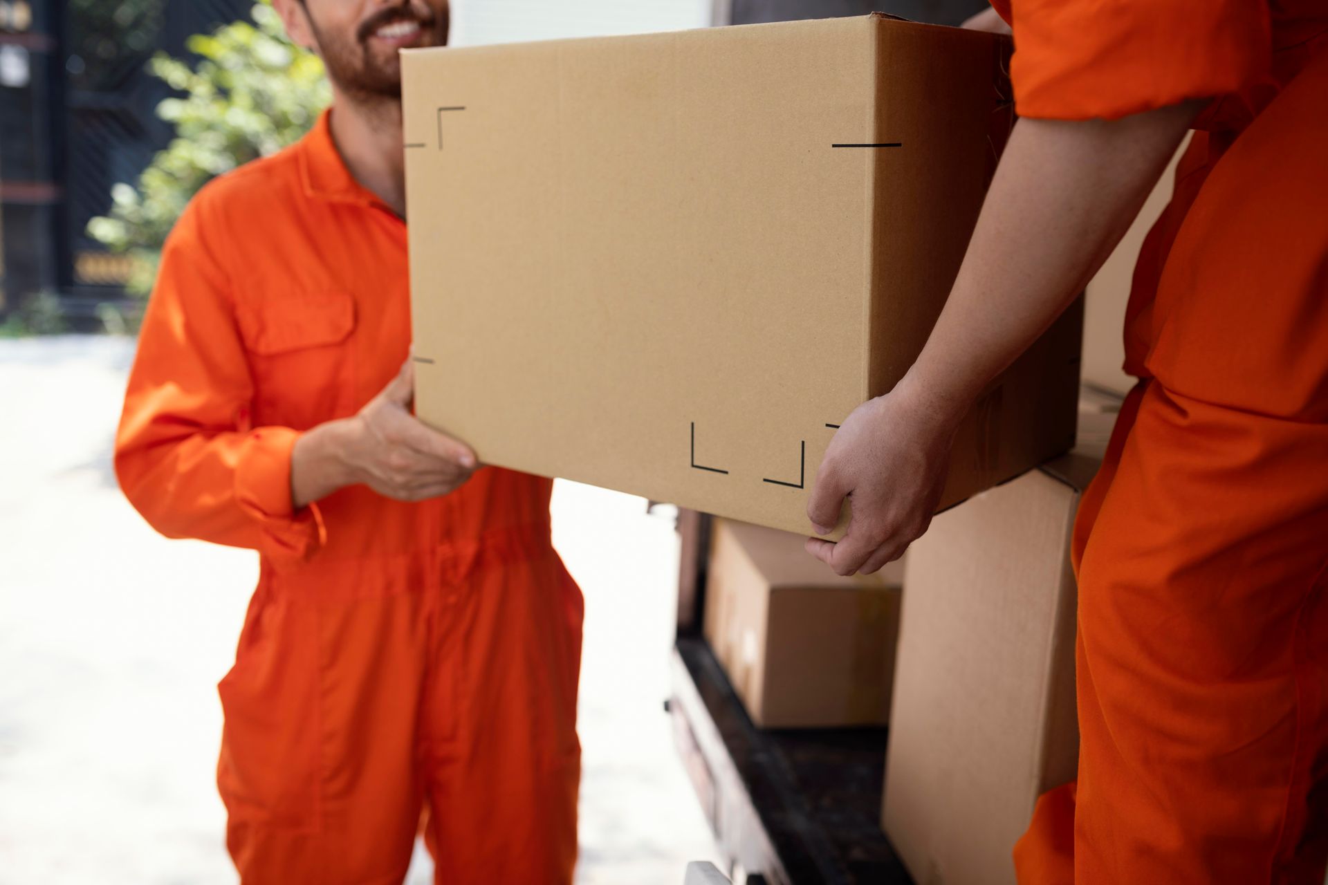 Two people in orange jumpsuits loading a cardboard box into a van.