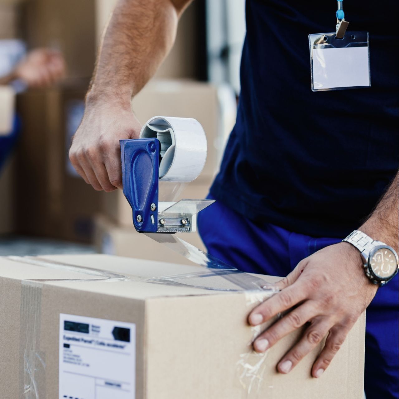 A man is taping a box with a blue tape dispenser
