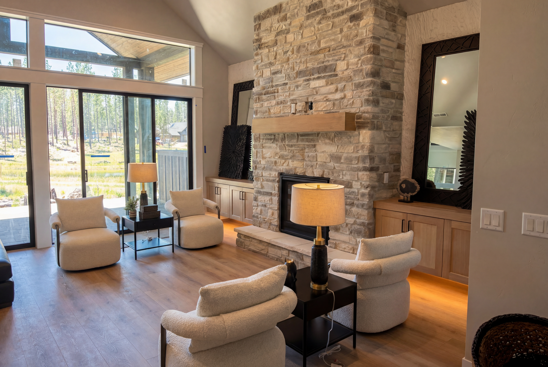 Living room with stone fireplace, wood floors, four white armchairs, and large windows.