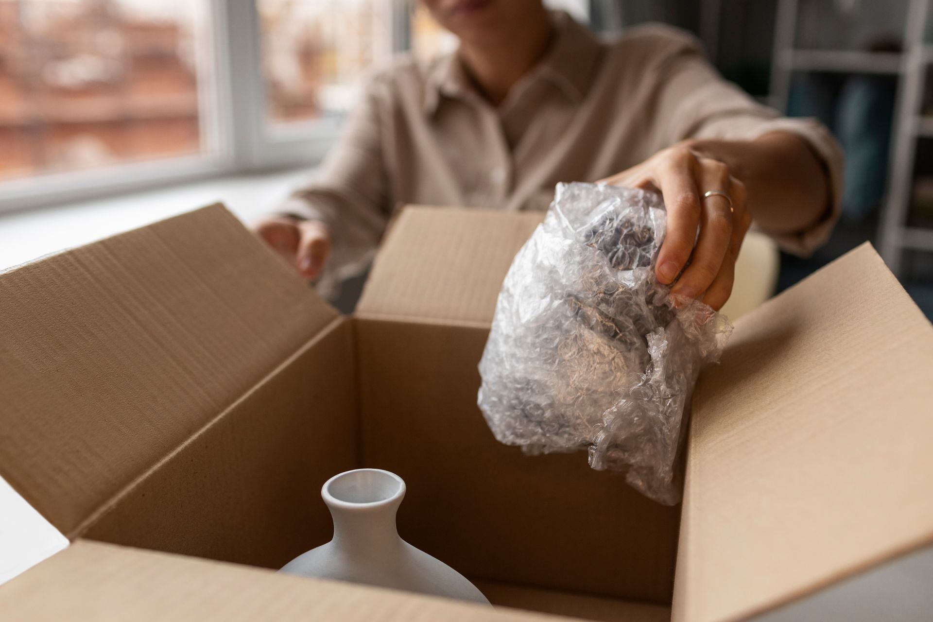 A woman is packing a vase in a cardboard box.