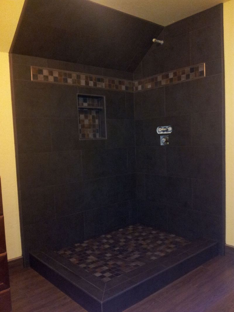 Dark tiled shower with stone floor and decorative border.