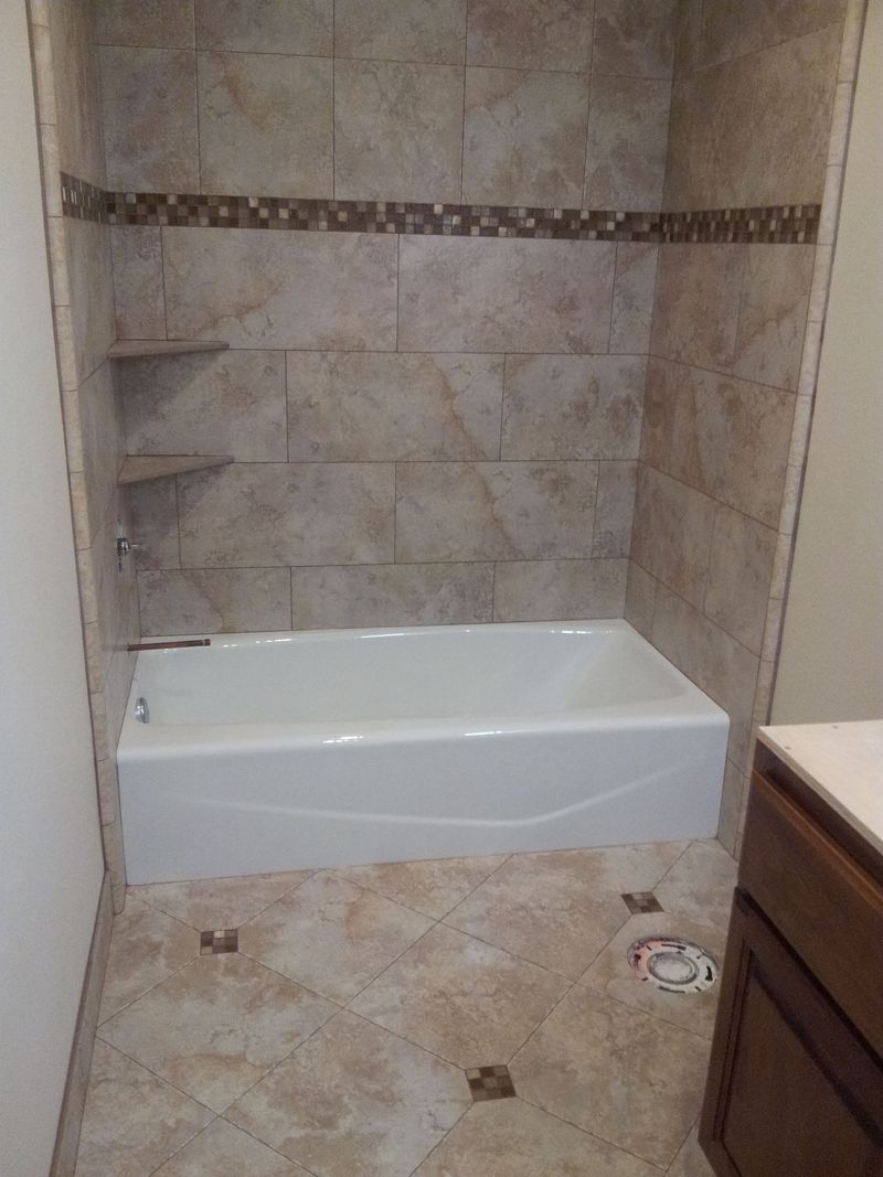 Bathroom with white bathtub, tiled walls, and floor. Built-in shelves and a decorative tile border.
