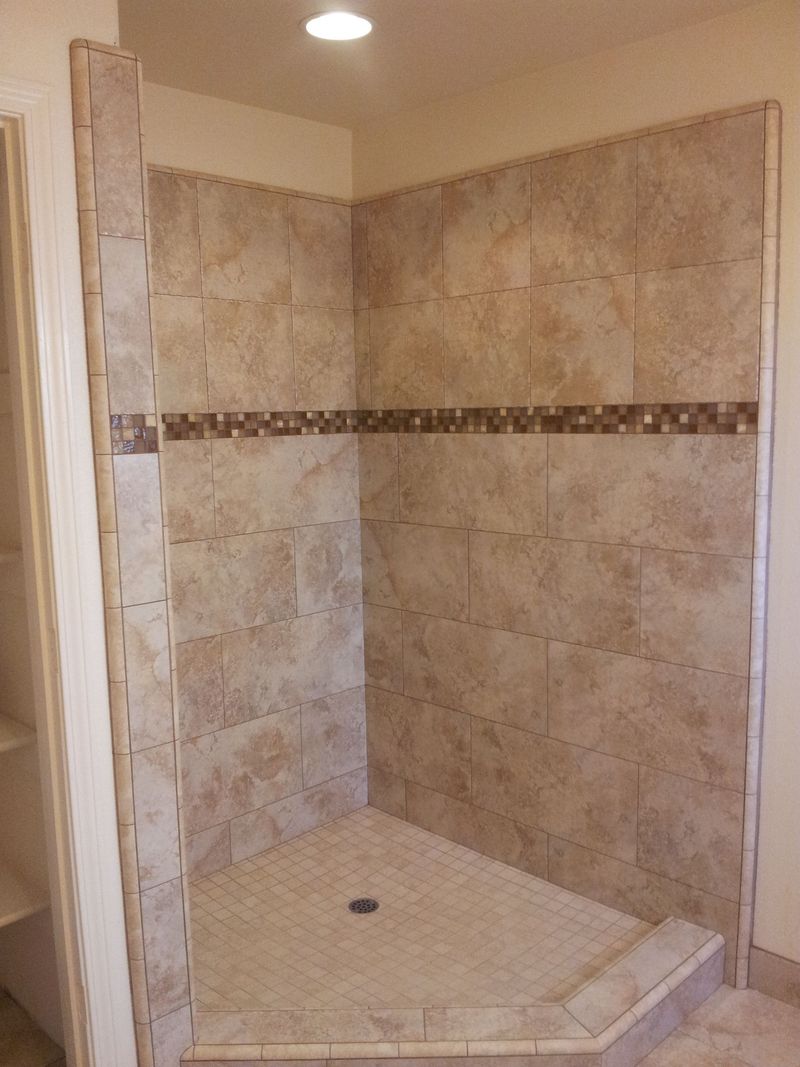 Shower with beige tile walls, mosaic accent, and angled base.