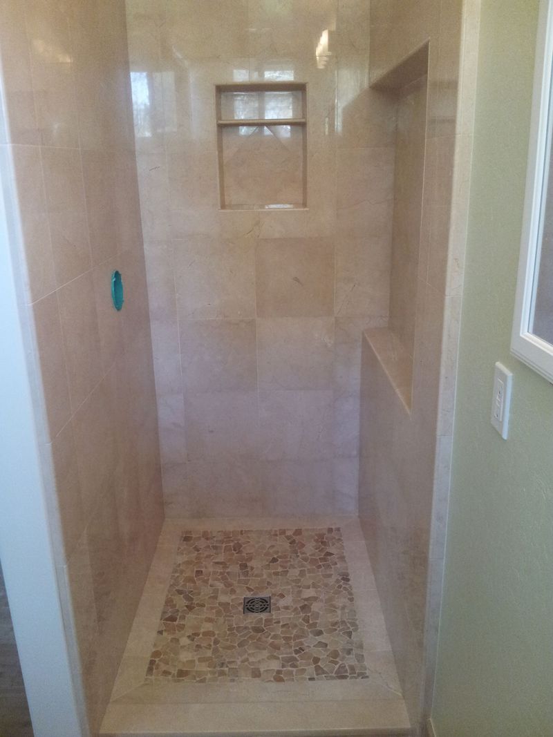 Shower with light beige tile walls, pebble floor, and built-in shelf.