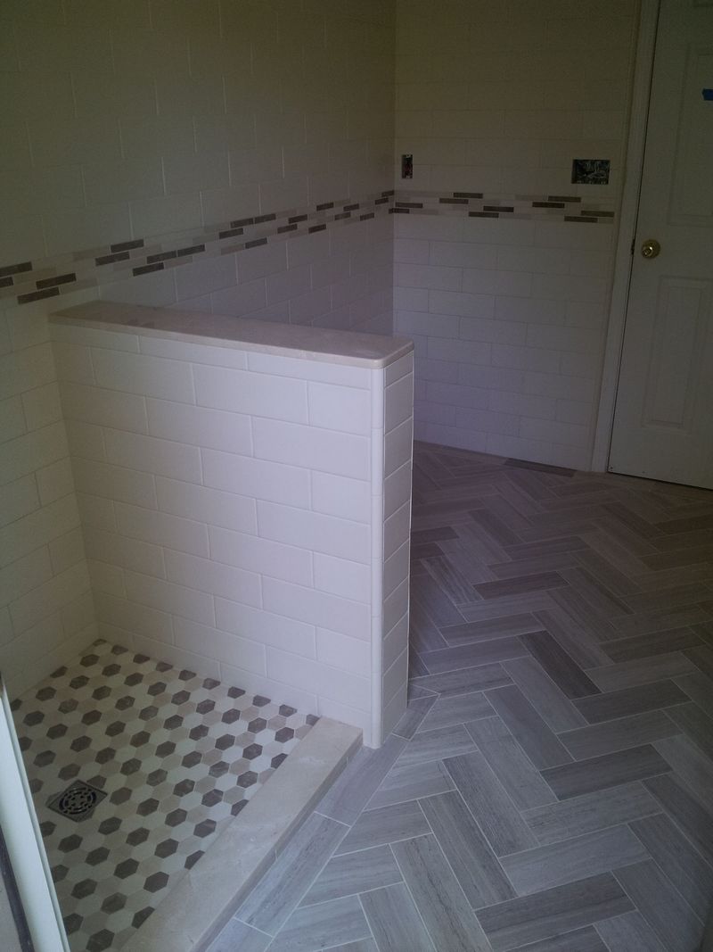 Bathroom under construction; shower with white and gray tile, herringbone floor, small decorative strip.