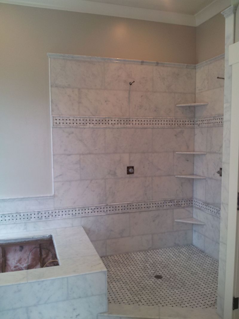 Marble-tiled shower with built-in shelves.  Small mosaic tiles on the floor.  Neutral colored walls.