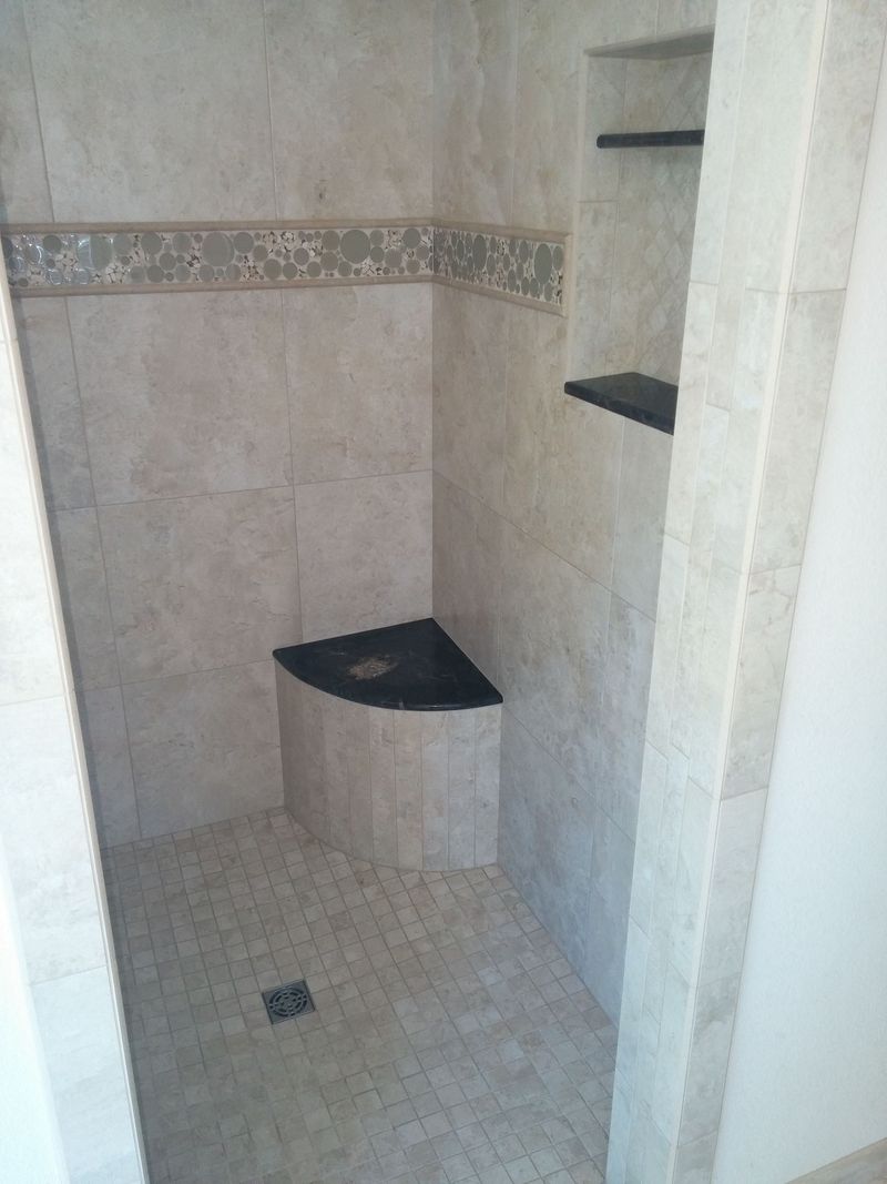 Tiled shower with corner seat and built-in shelves; neutral beige and brown tones.