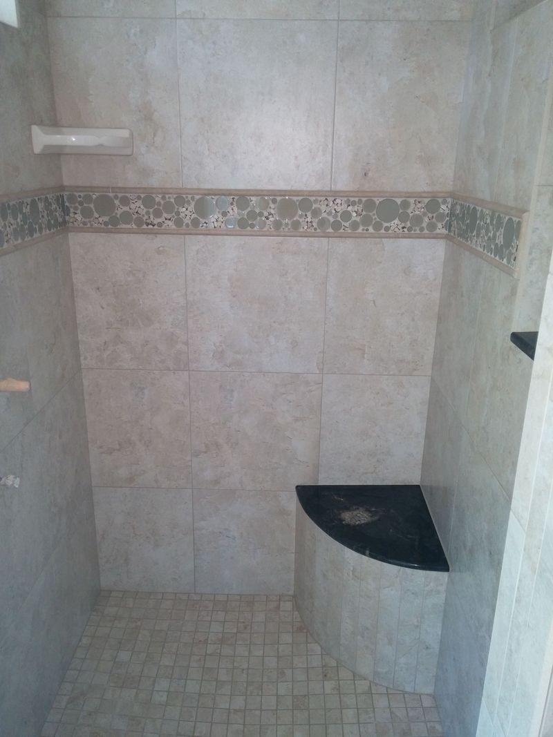 Tiled shower stall with a built-in black corner seat and a decorative tile border.