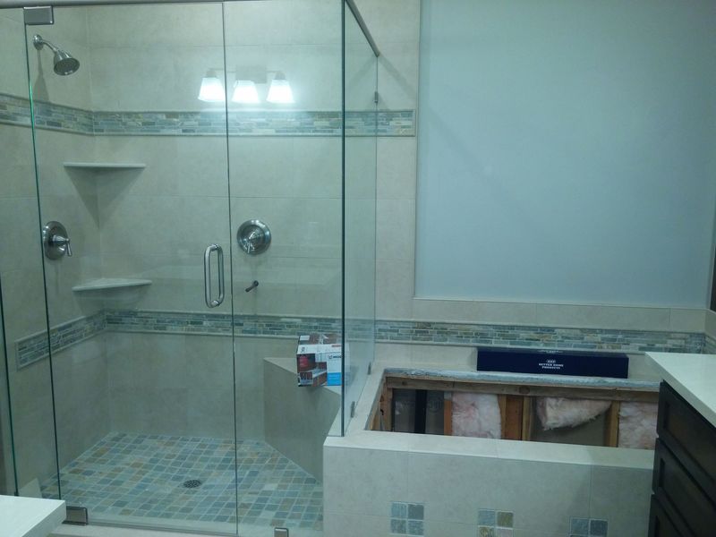 Bathroom with glass shower, tiled walls, and exposed tub area.