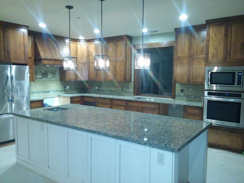 Kitchen with white island, wood cabinets, granite countertops, stainless steel appliances, and pendant lights.