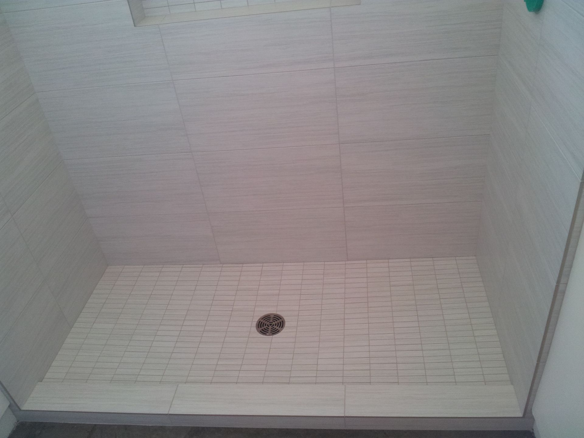 Empty shower stall with light-colored tile walls and floor, and a central drain.