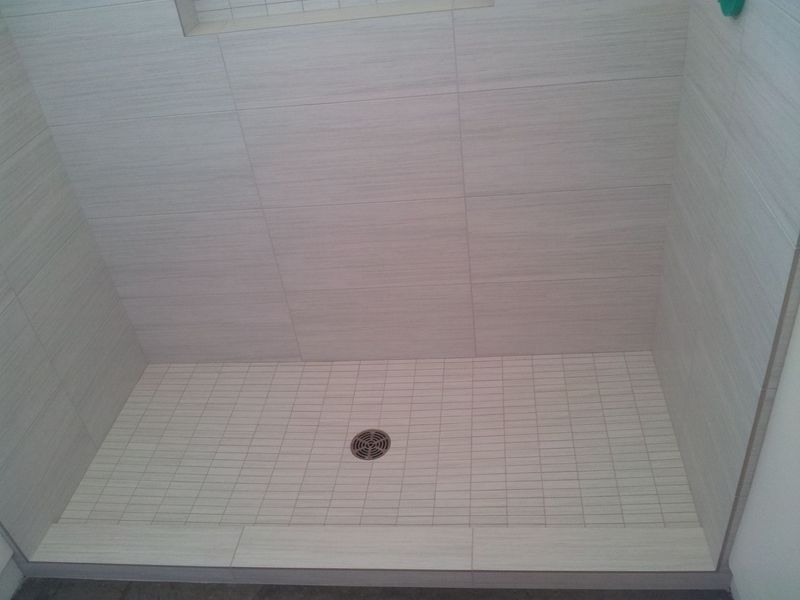 Empty shower stall with light-colored tile walls and floor, and a central drain.