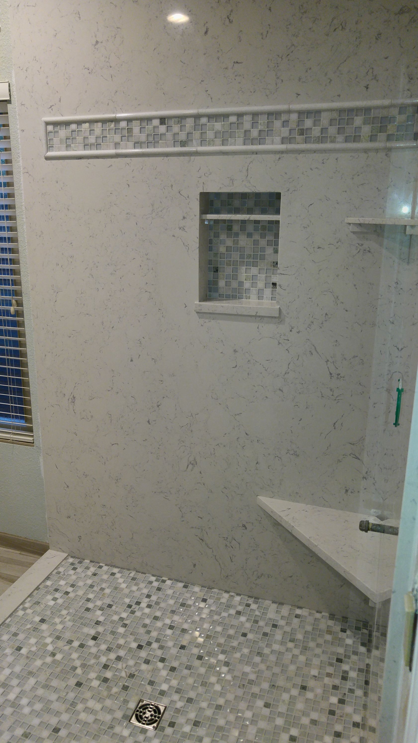 Shower with mosaic tile floor and walls, built-in bench, and niche. Glass door on right.