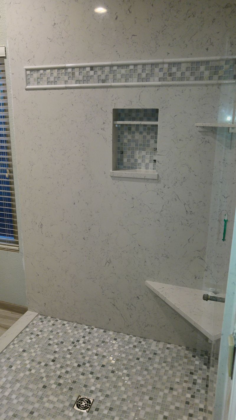 Shower with mosaic tile floor and walls, built-in bench, and niche. Glass door on right.