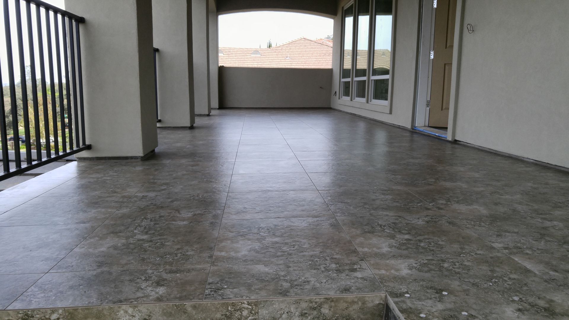 Balcony with grey tile floor, railings, columns, and windows, overlooking a landscape.