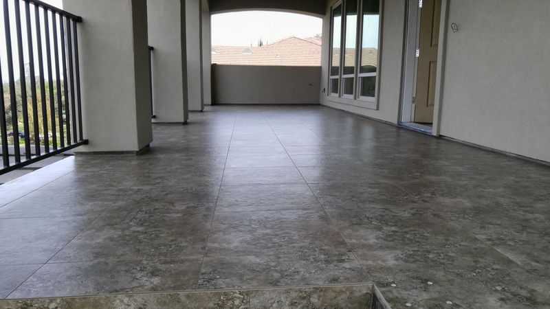 Balcony with grey tile floor, railings, columns, and windows, overlooking a landscape.
