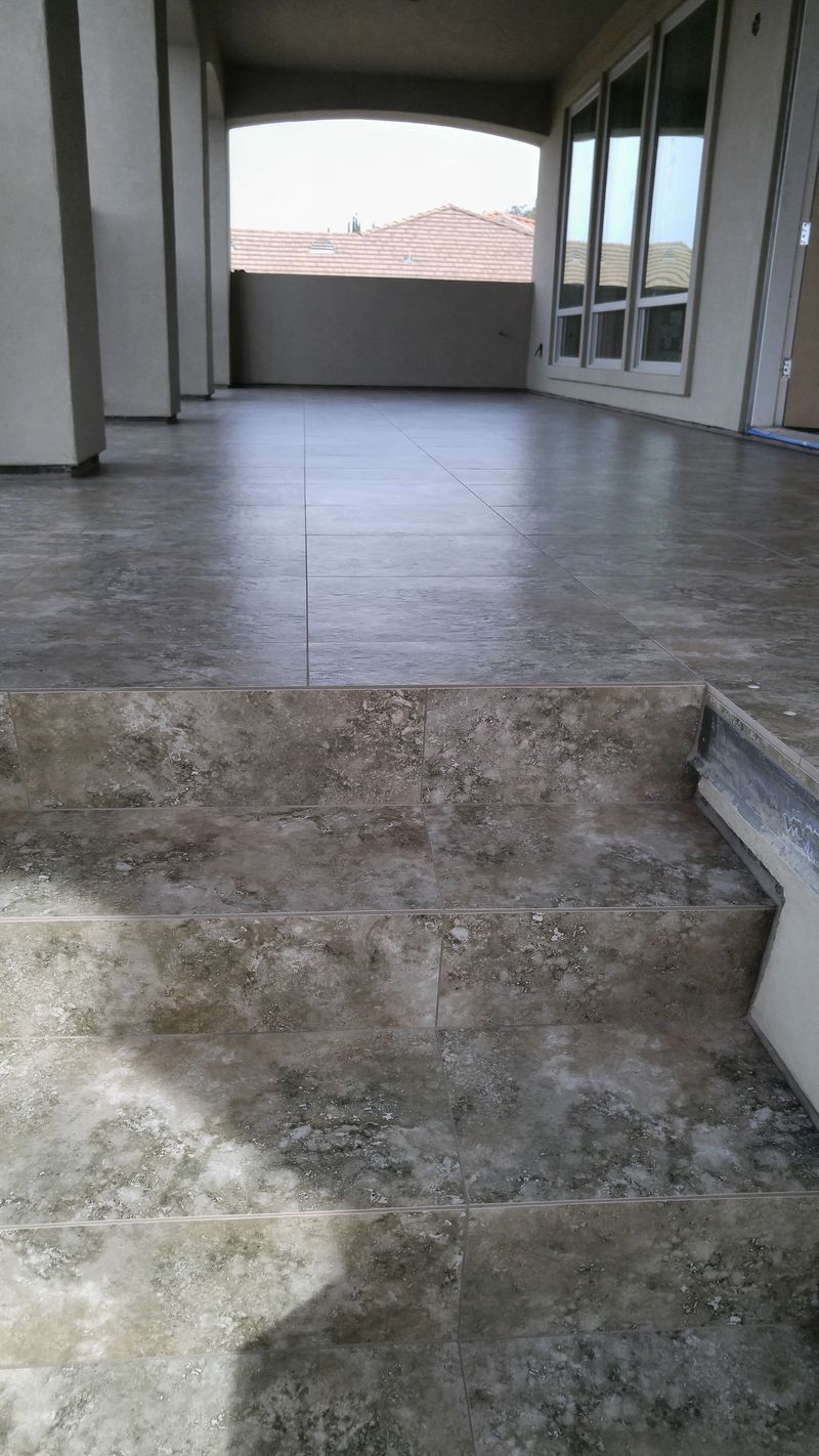 Stone steps leading up to a covered patio with a concrete floor, surrounded by walls and large windows.