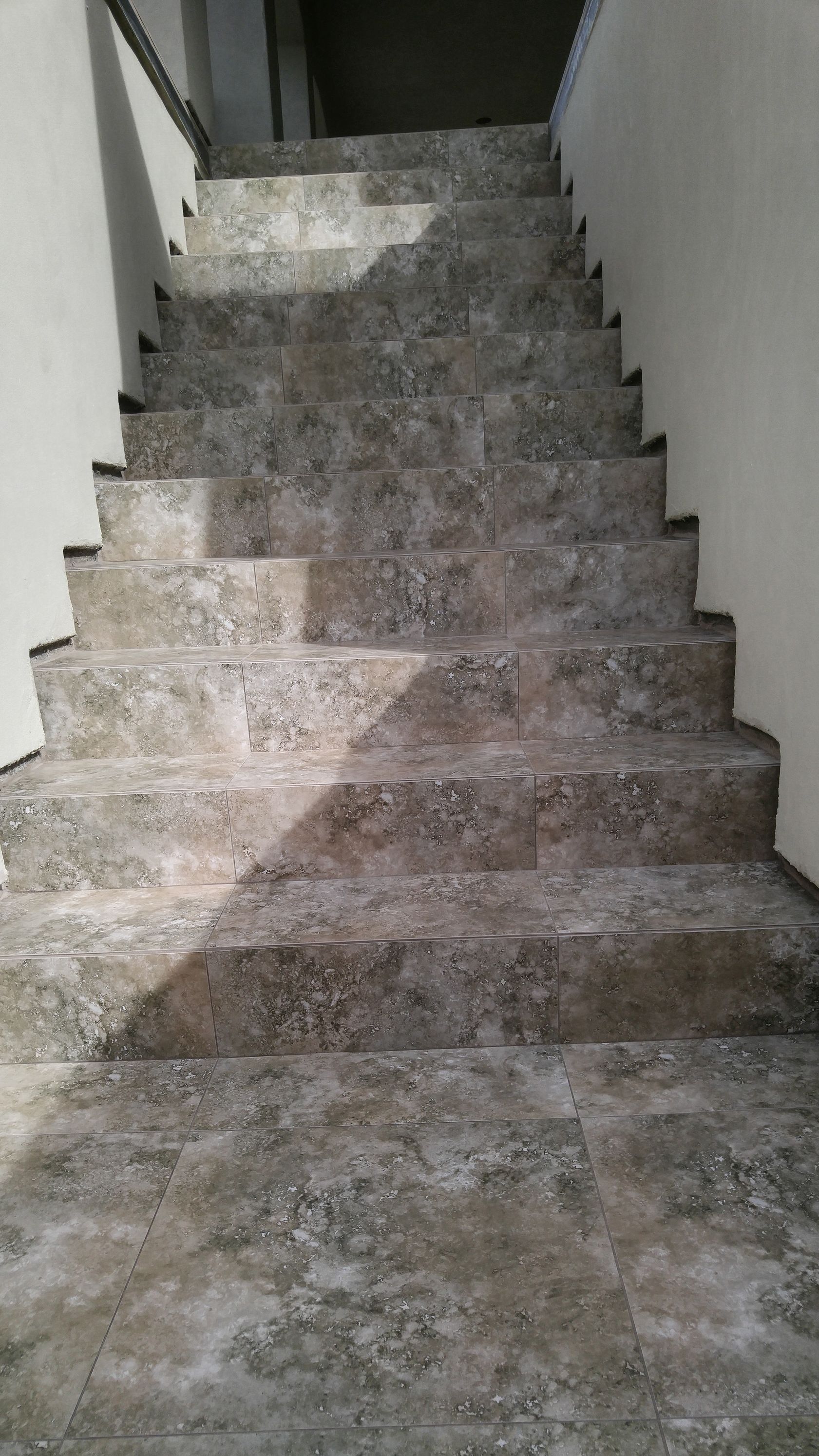 Concrete staircase, leading upwards. Gray and white speckled, with simple white walls on either side.
