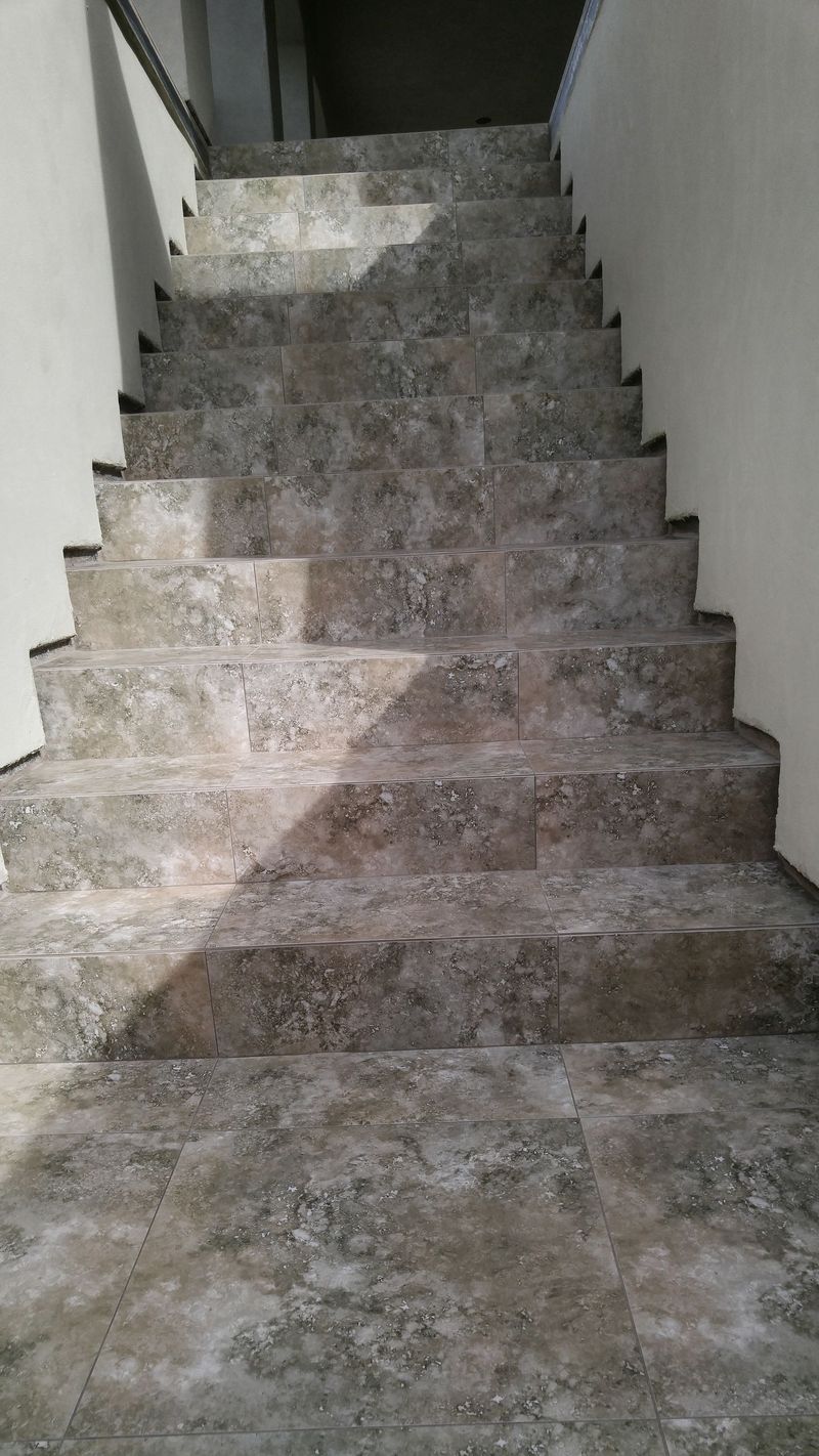 Concrete staircase, leading upwards. Gray and white speckled, with simple white walls on either side.