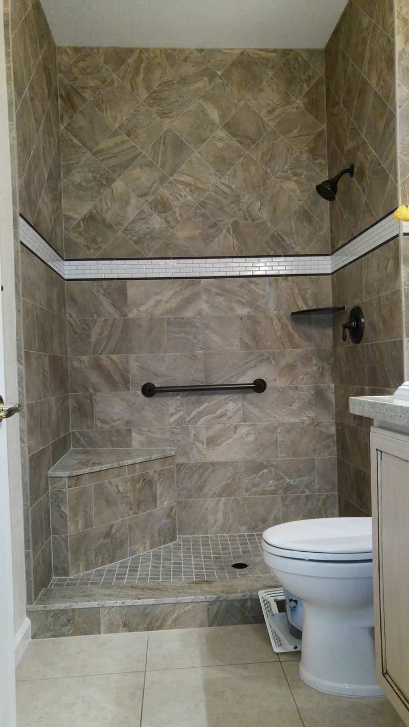 Tiled shower with grab bar, built-in seat, and toilet. Brown tiles with a white stripe.