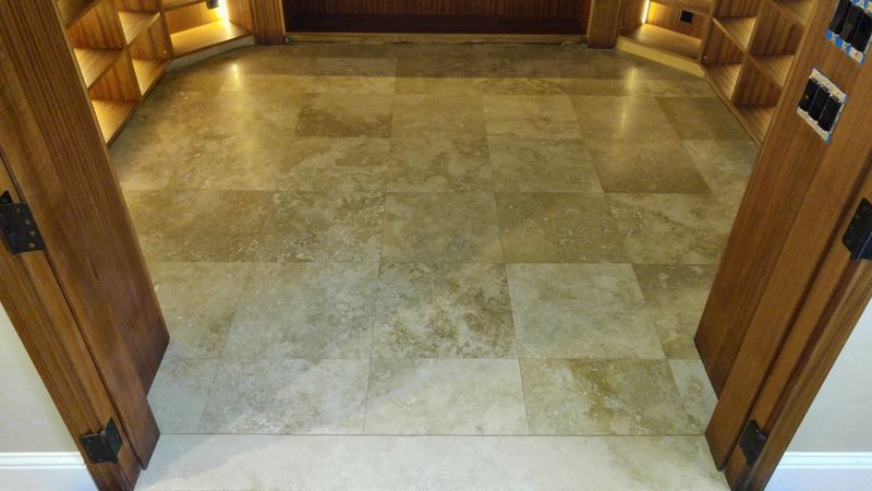 Stone tile floor inside a room with wooden door frames and shelves illuminated by warm lighting.