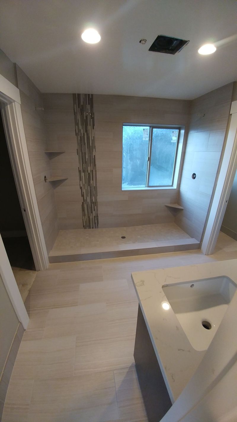Bathroom with tiled walls, shower, vanity, and window. Beige and brown tones.