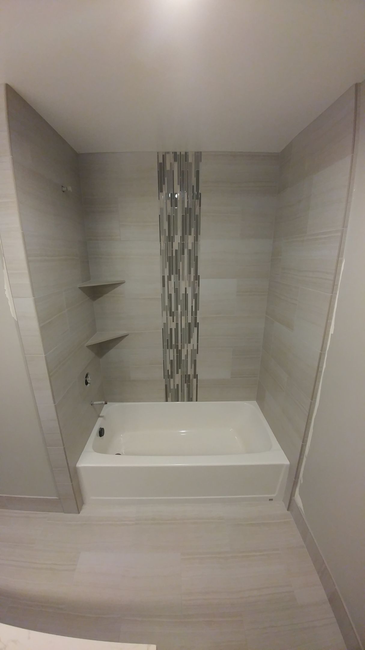 Bathroom with a rectangular tub, tiled walls, and shelves. Neutral colors, modern design.