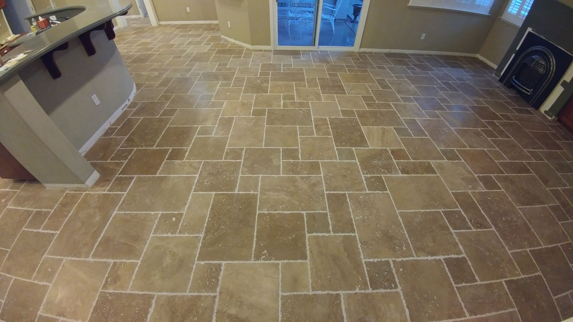 Tiled floor in a room with a sliding glass door and kitchen island. Light brown tiles are arranged in a random pattern.
