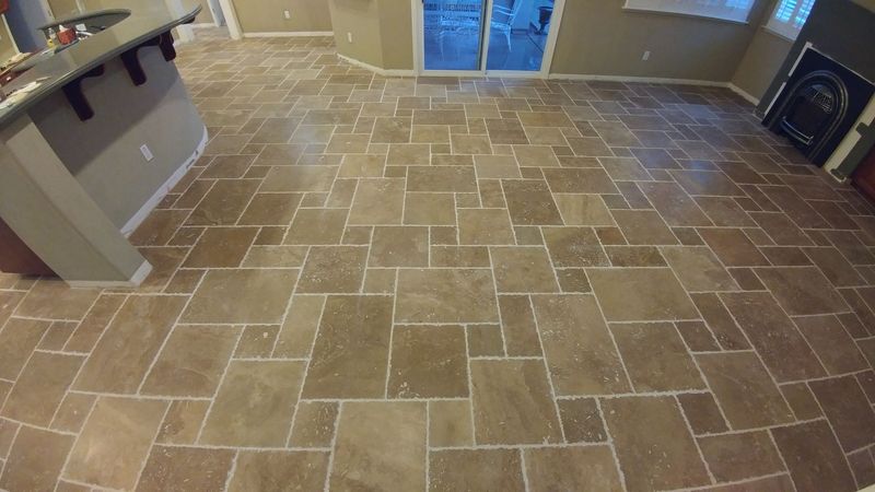Tiled floor in a room with a sliding glass door and kitchen island. Light brown tiles are arranged in a random pattern.