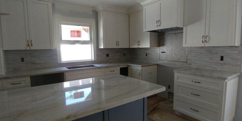 White kitchen with granite countertops and island, cabinets, and a window.