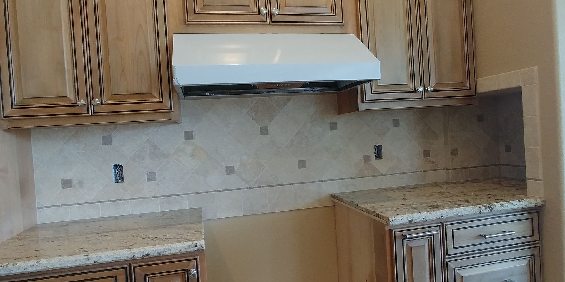Kitchen with wooden cabinets, granite countertops, and tiled backsplash under a range hood.