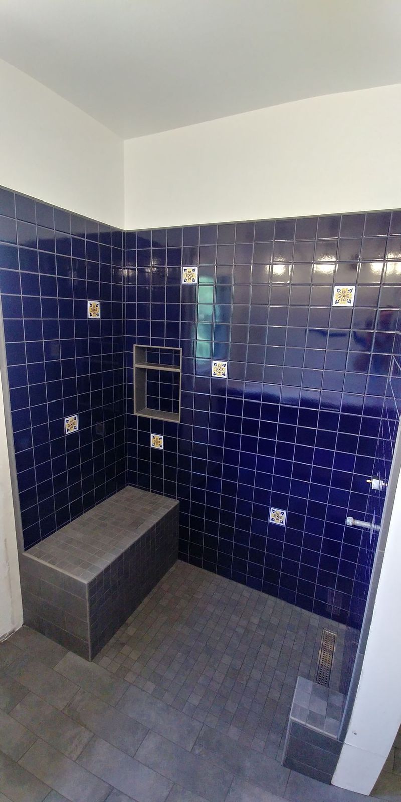 Blue-tiled shower with a built-in bench. The walls and floor are dark gray.