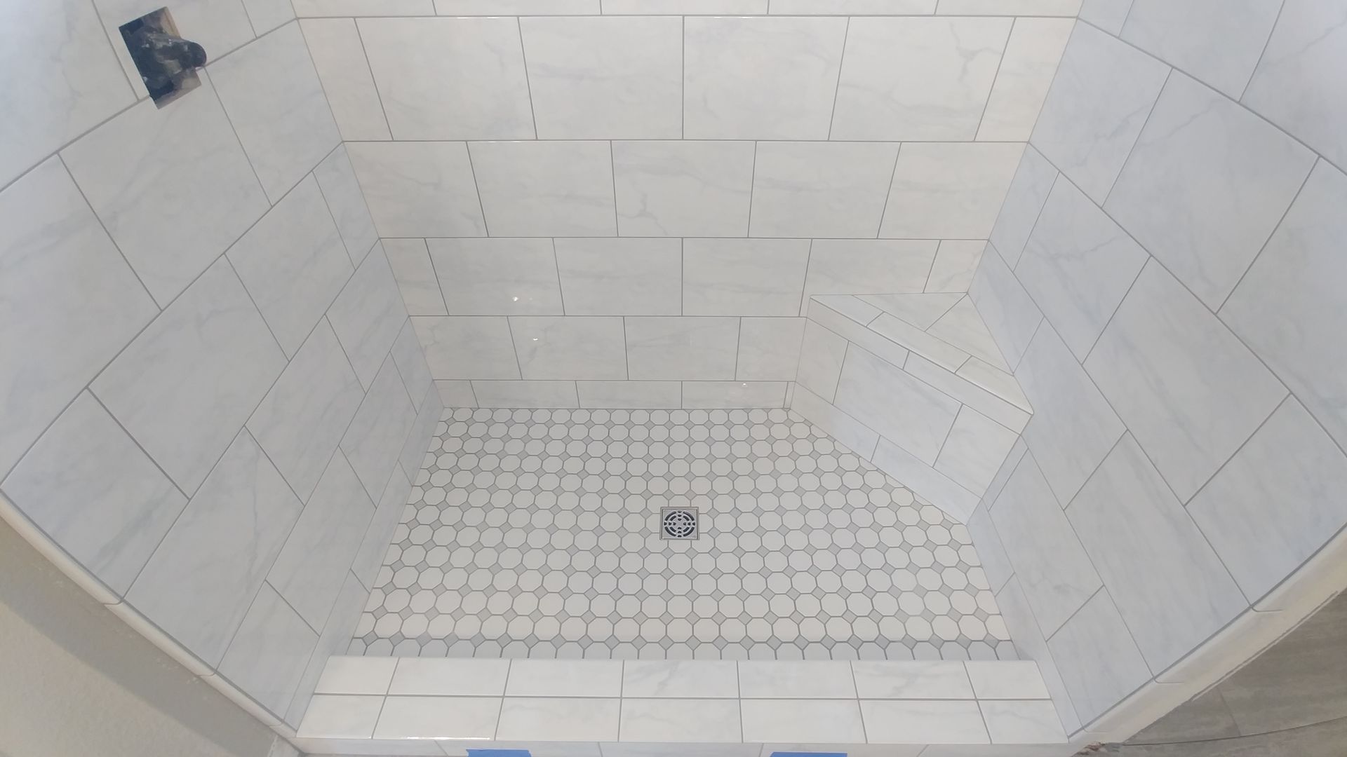 Tiled shower stall in progress with a center drain, white tiles, and grey grout.