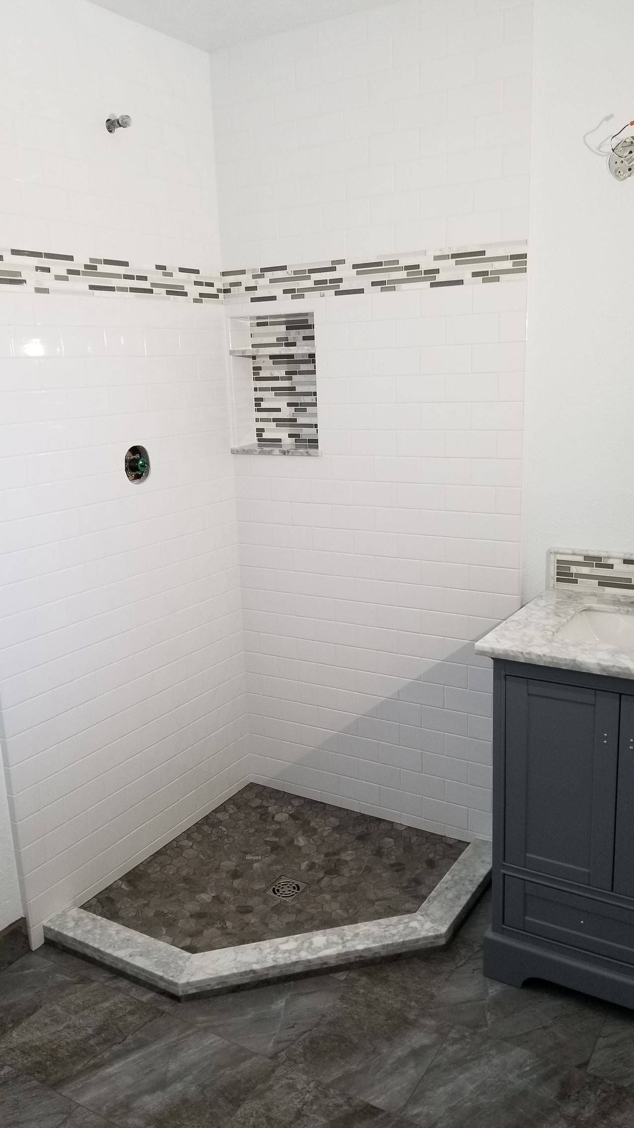 Bathroom with white walls, tiled shower with dark pebble floor, gray vanity.