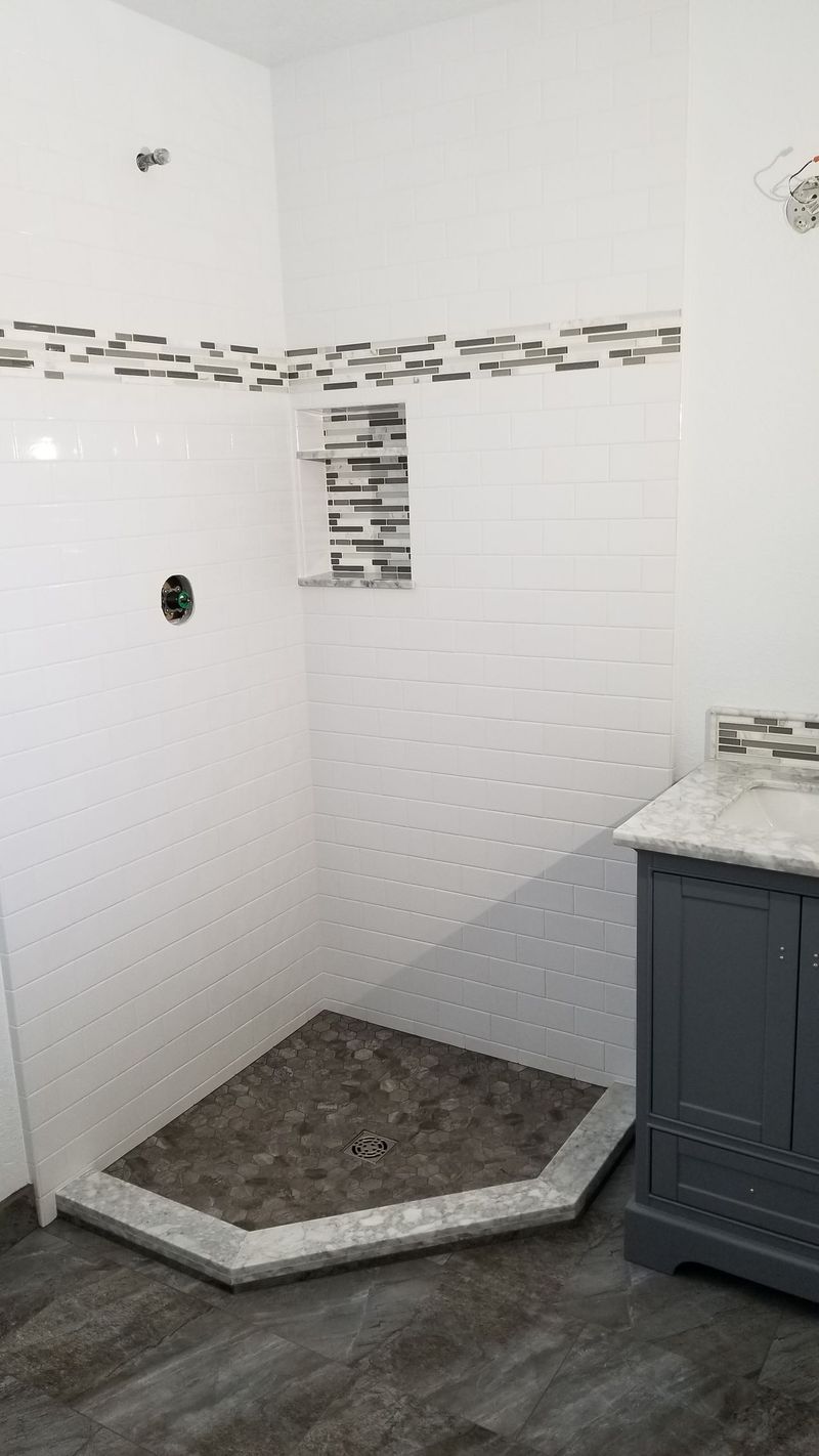 Bathroom with white walls, tiled shower with dark pebble floor, gray vanity.