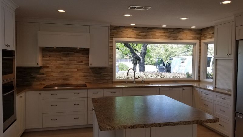 Modern kitchen with white cabinets, stone backsplash, island with granite countertop, and a window.