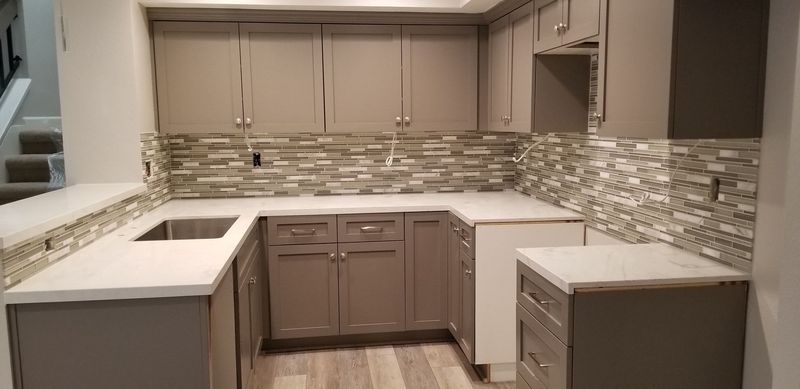 Kitchen with gray cabinets, white countertops, and a stone backsplash.