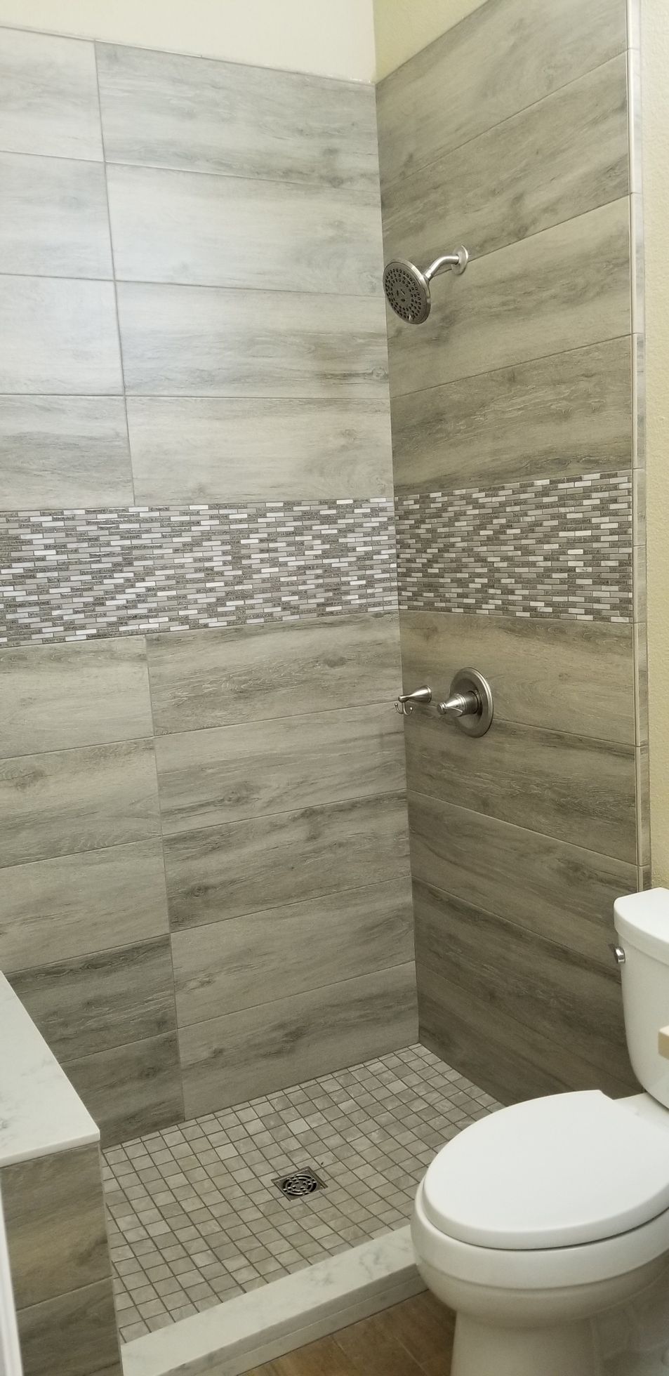 Shower stall with gray marbled tiles, a mosaic tile band, and a toilet.