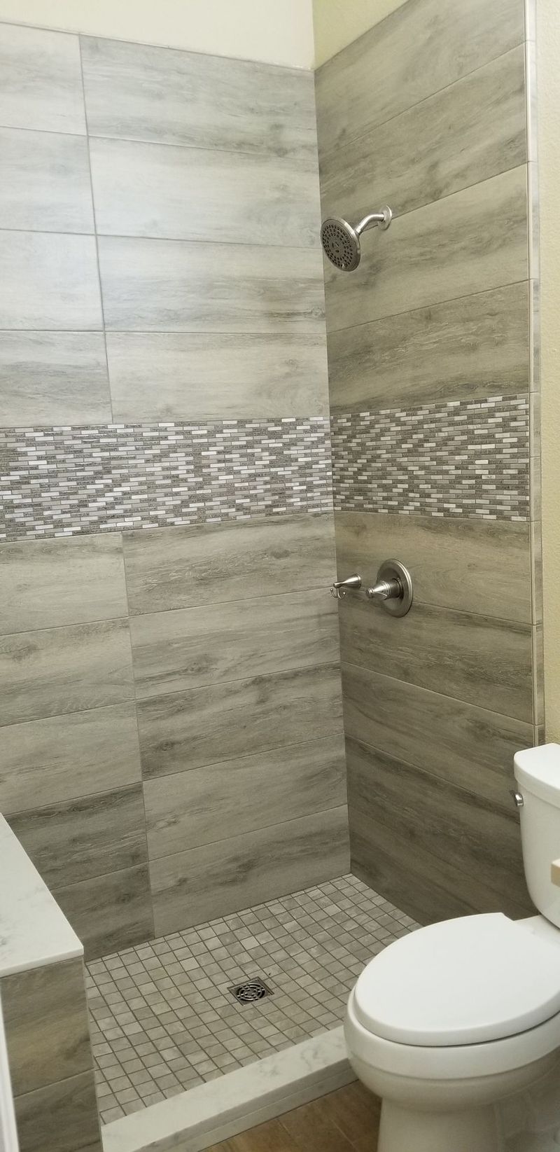Shower stall with gray marbled tiles, a mosaic tile band, and a toilet.