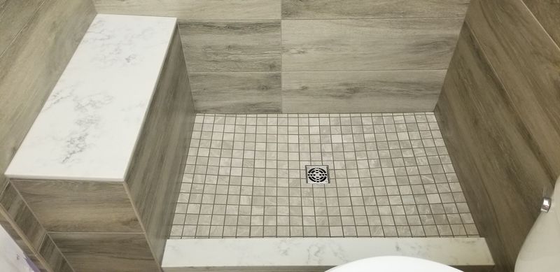 Tiled shower with a bench, square tile floor, and neutral-colored walls.
