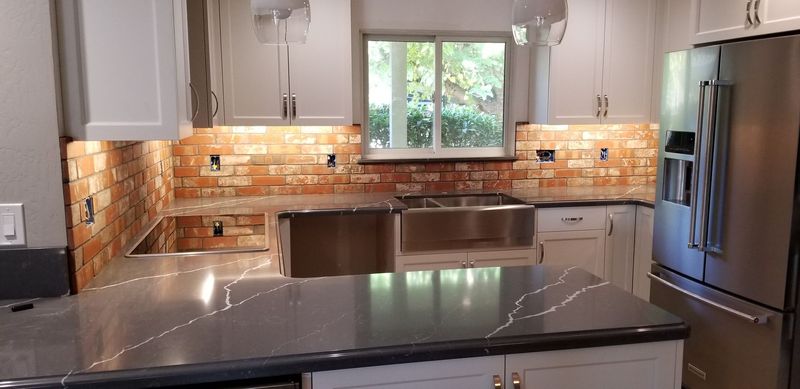 Kitchen with grey countertops, brick backsplash, stainless steel sink, and refrigerator.