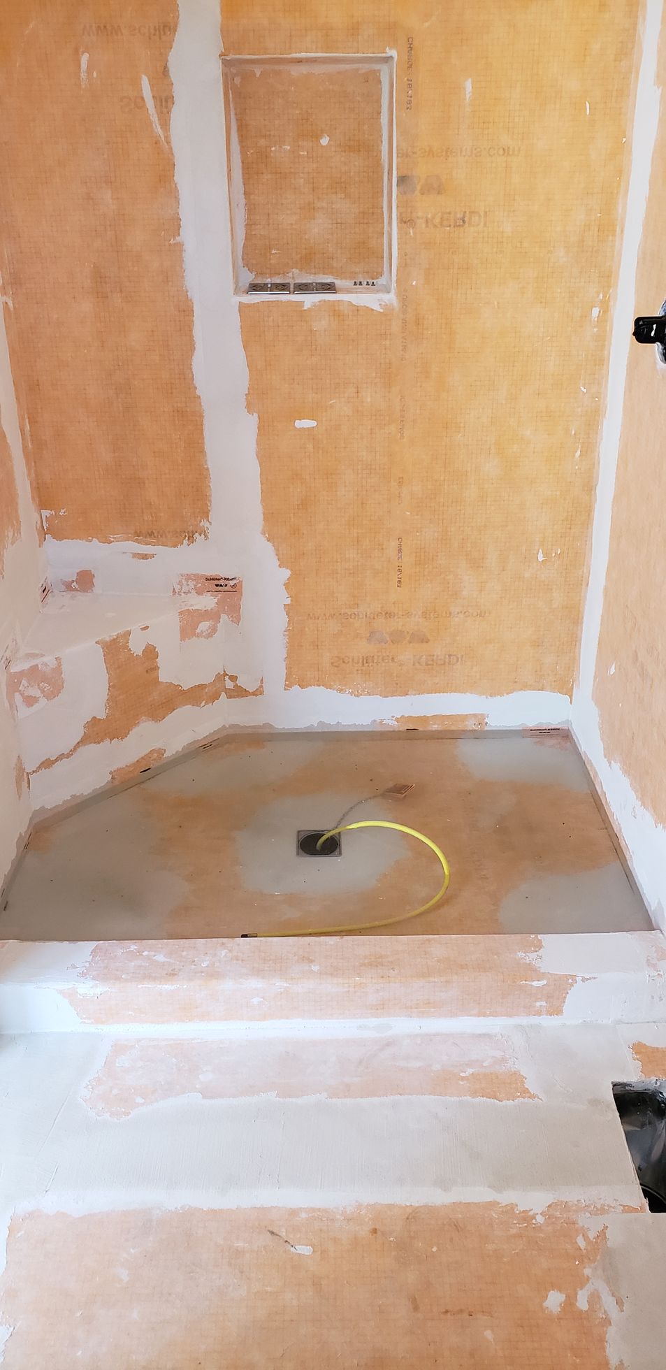 Shower stall under construction, with backer board on the walls, and a drain visible in the shower pan.