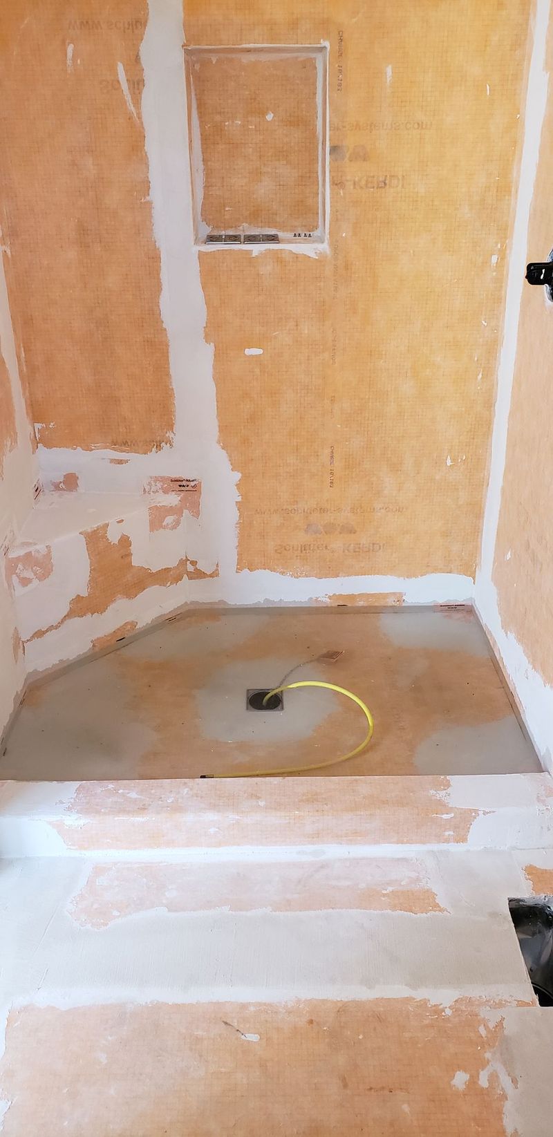 Shower stall under construction, with backer board on the walls, and a drain visible in the shower pan.