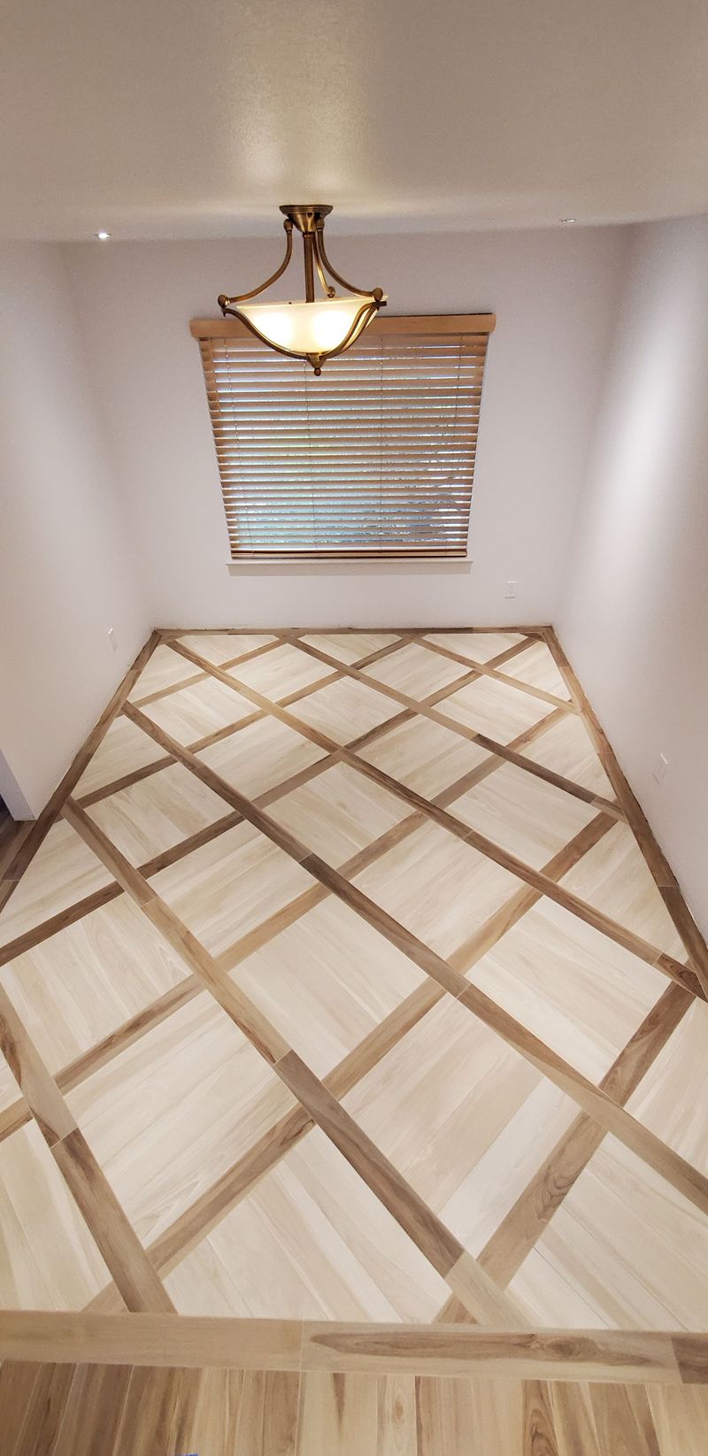 Room with a diamond pattern wood floor, wall blinds, and a light fixture.
